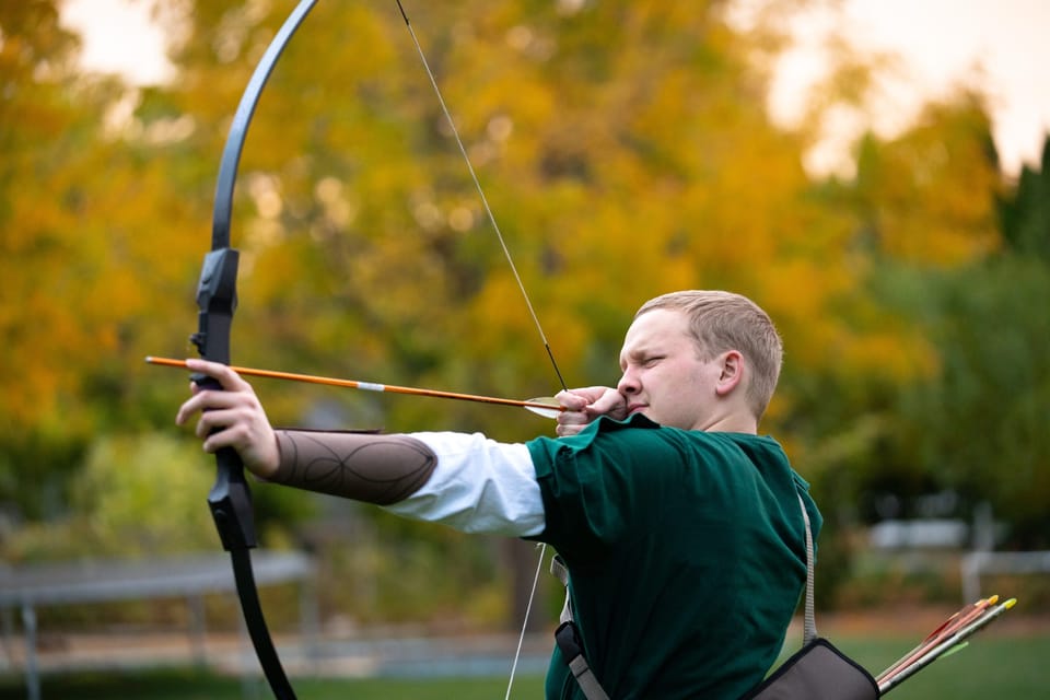 Archer drawing a bow in front of golden autumn trees