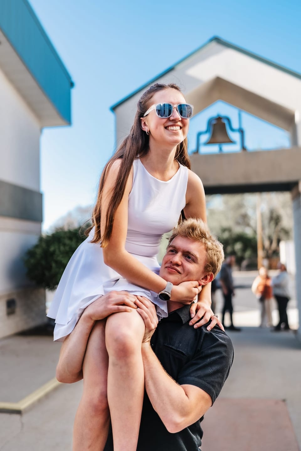 Woman sitting on her partner's knee in front of a bell tower