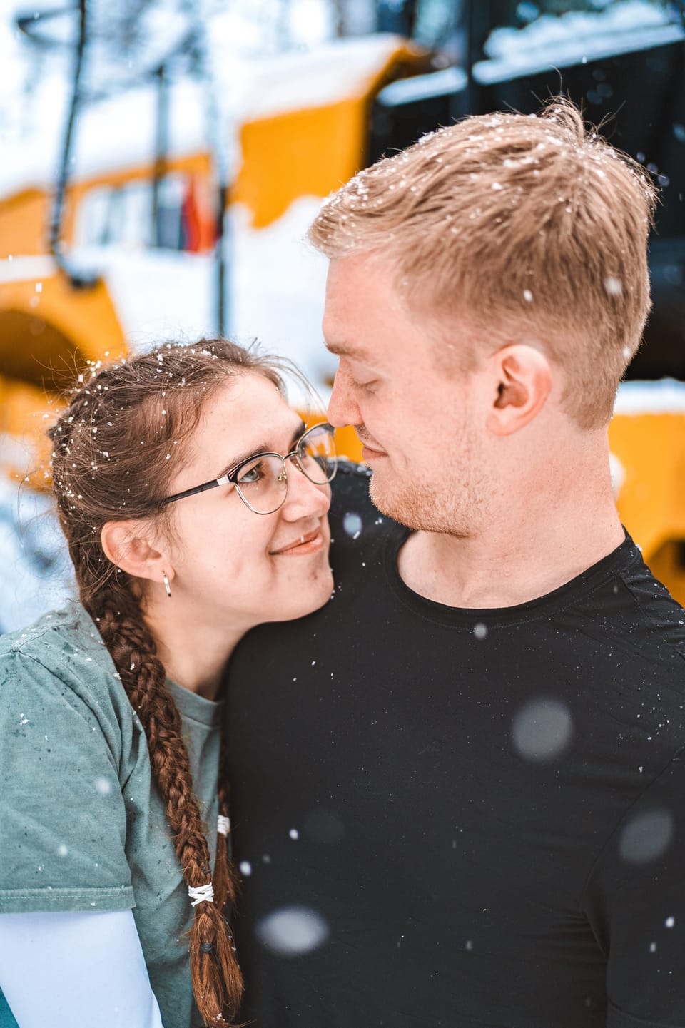 Couple smiling close together as snow falls around them