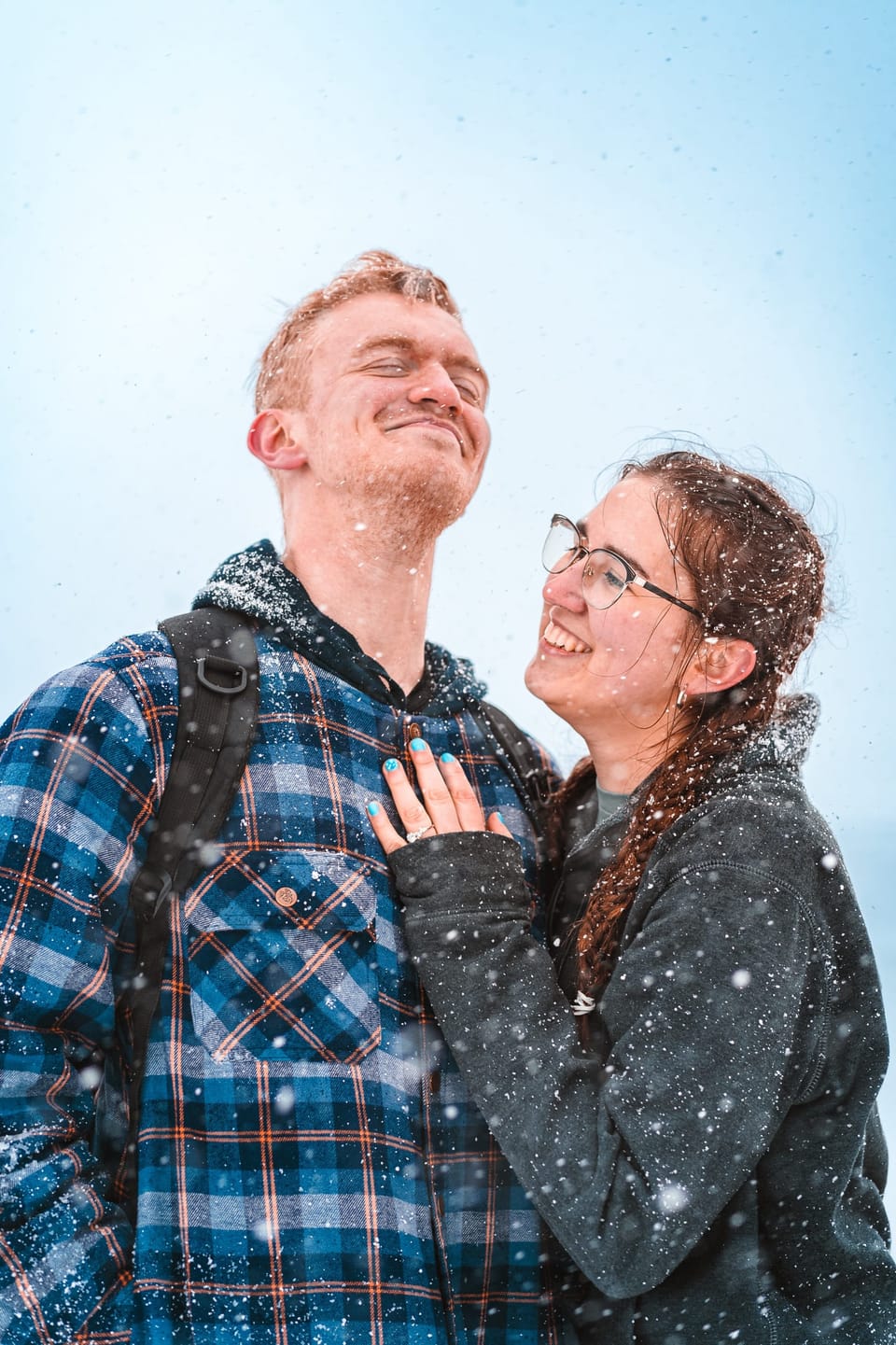 Couple in flannel and a knit sweater hugging on a sunny winter day