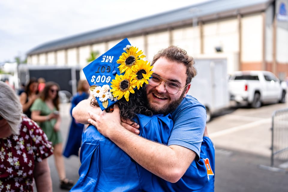 Graduate holding sunflowers while hugging a friend
