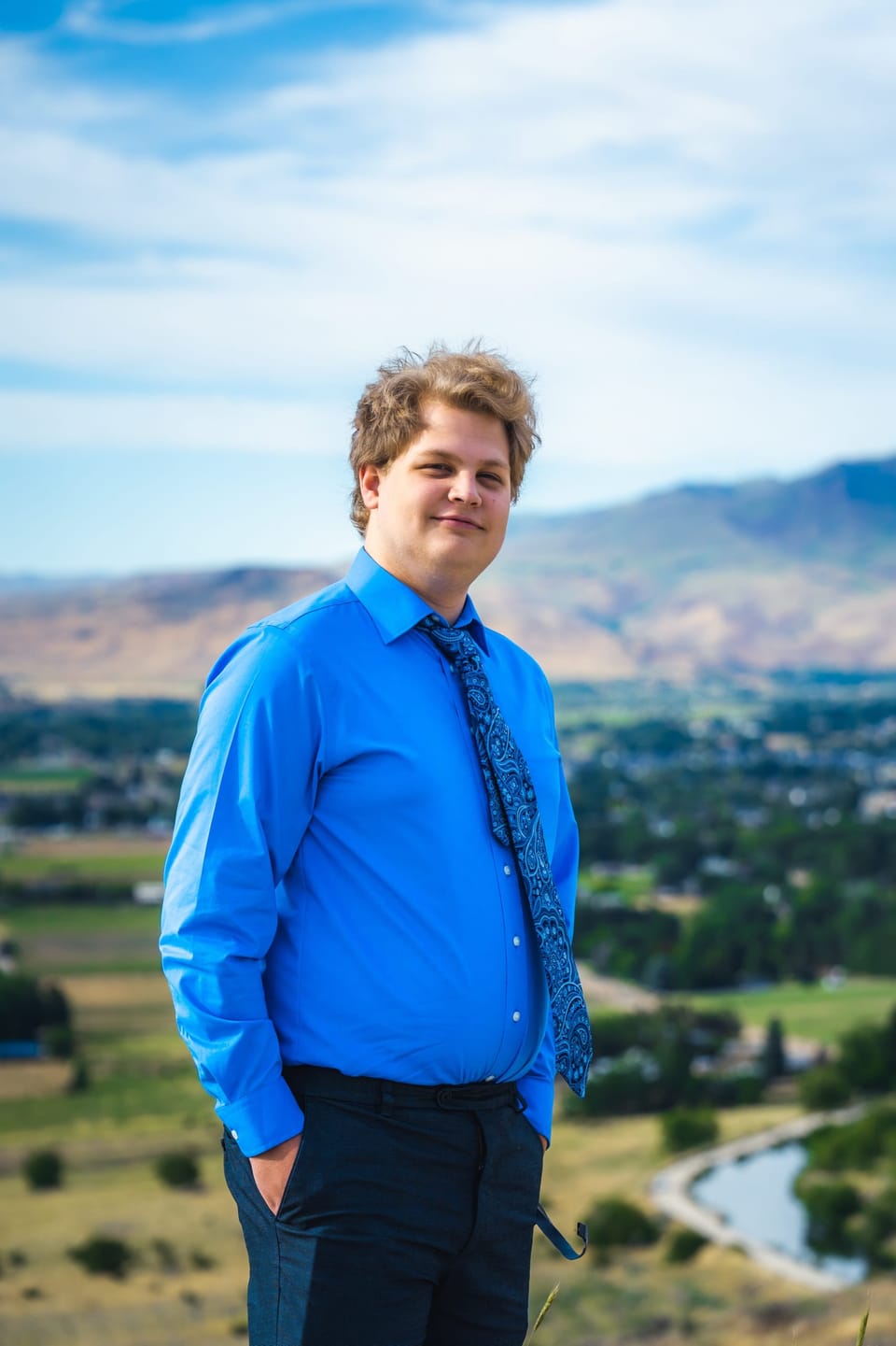 Man in a blue dress shirt standing above a green valley