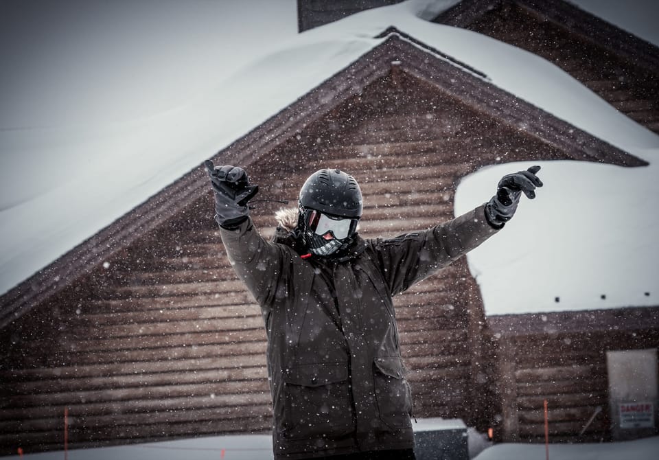Man in a camo jacket posing outside a wooden cabin