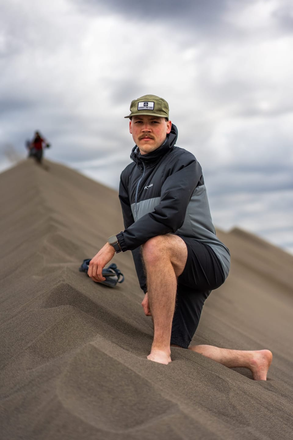Barefoot man in a cap kneeling on a sand dune