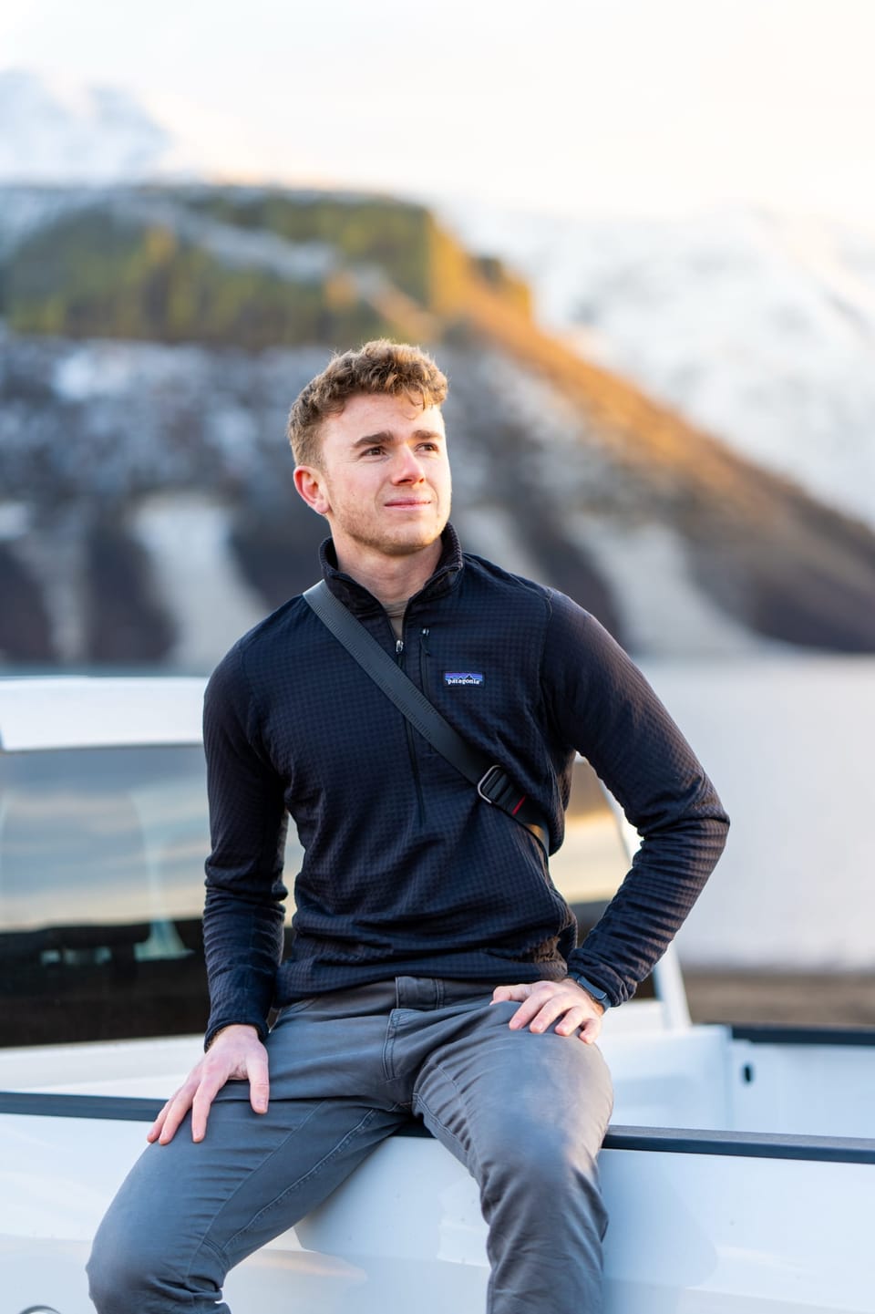 Young man sitting on a truck in a snowy mountain landscape