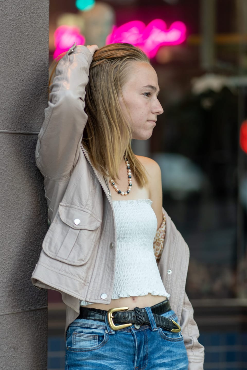 Young woman in a denim jacket posing under a glowing neon sign