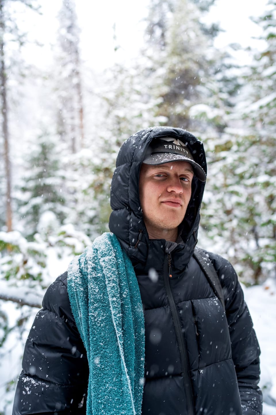 Man in a hooded parka and teal scarf in a snowy forest