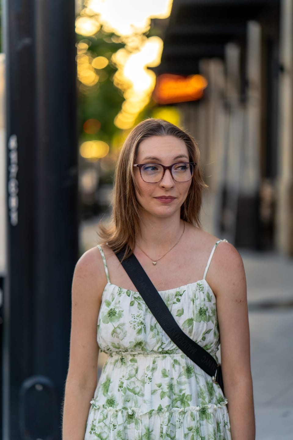 Woman in a floral sundress smiling on a downtown sidewalk