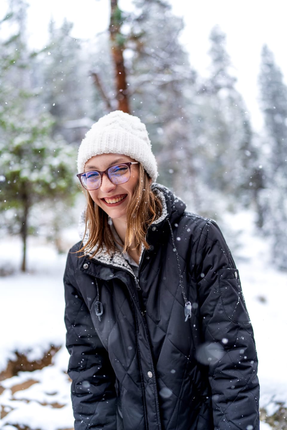 Smiling woman in a white knit hat in a snowy forest