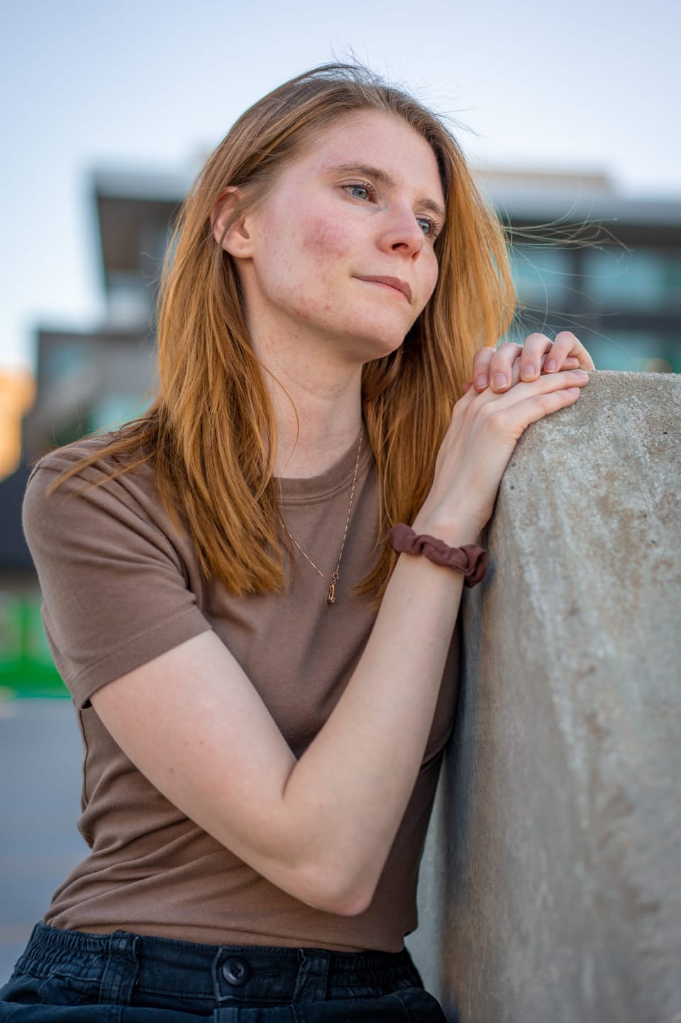 Woman in a brown top leaning on a wall with city buildings behind