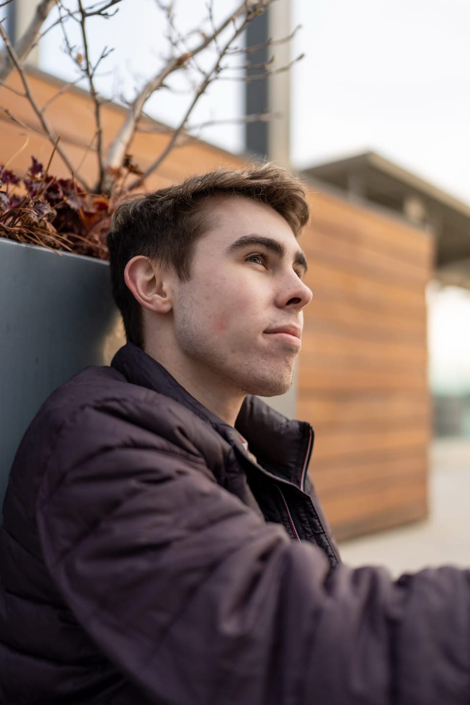 Young man in a dark jacket leaning against a wall