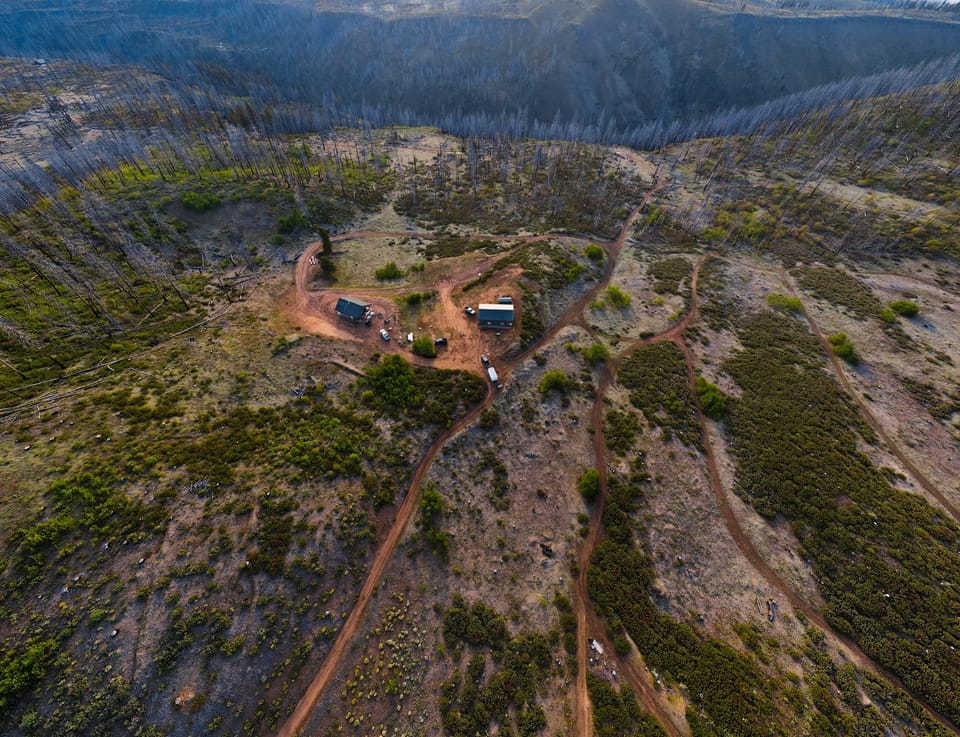 Aerial view of a winding dirt road through a sunlit mountain valley