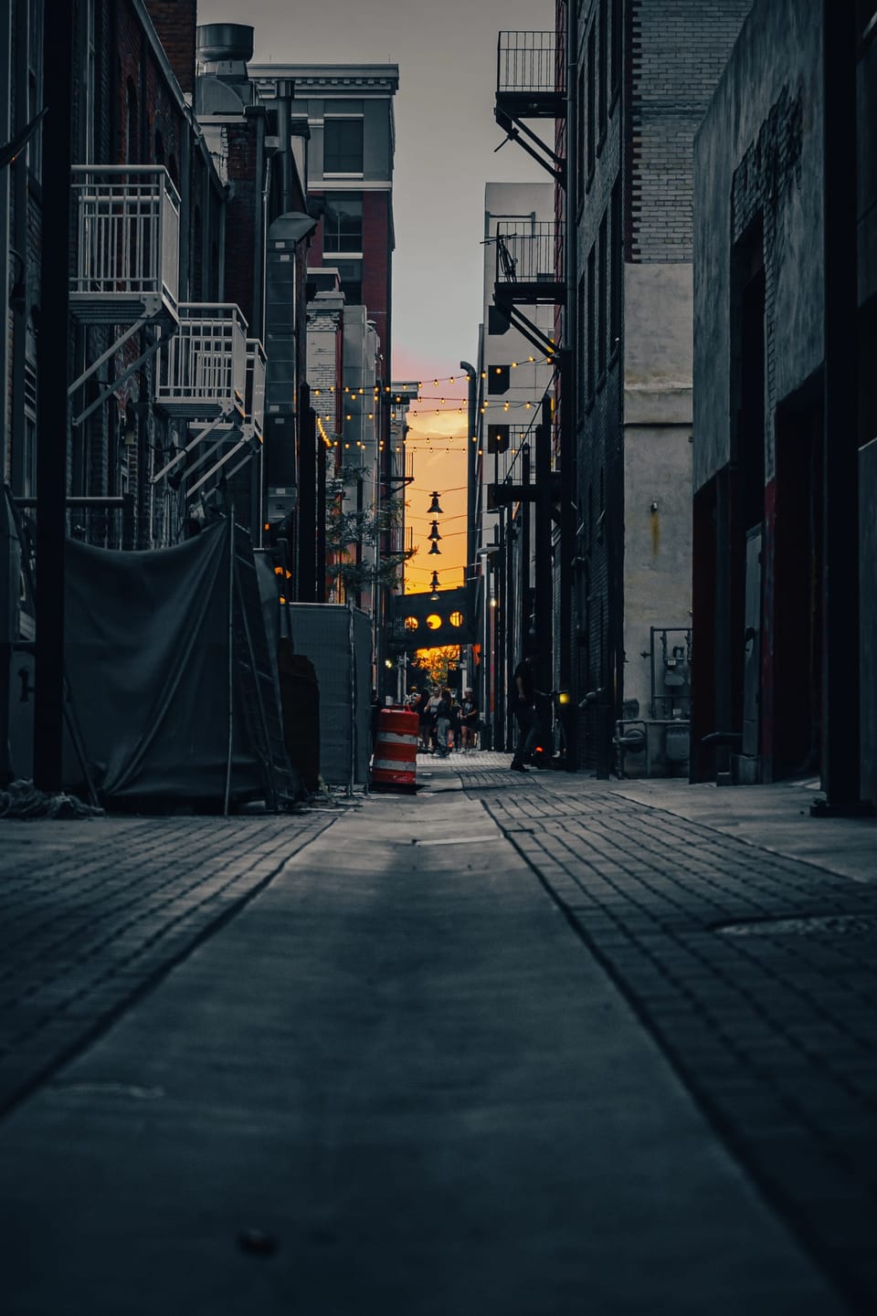 Narrow city alley between tall buildings with the setting sun at the far end