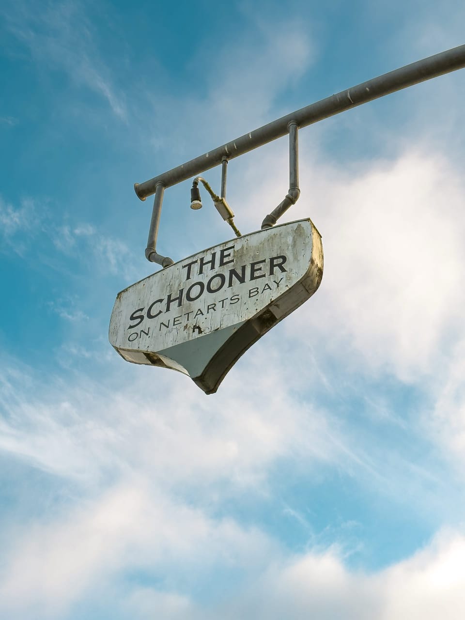 Weathered hanging sign against a blue sky with white clouds
