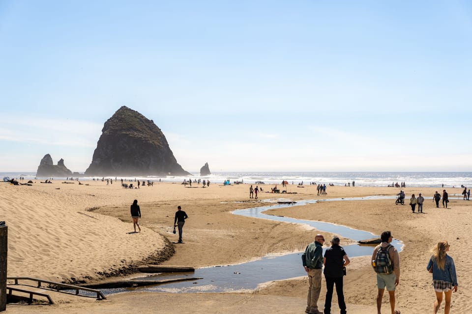 Beachgoers walking toward a large sea stack on a wide sandy beach