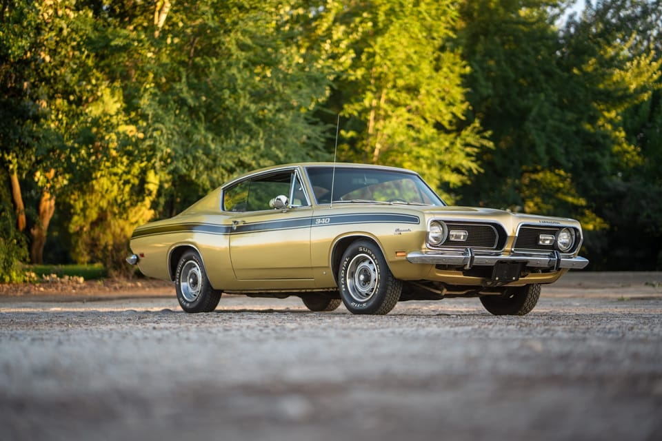 Gold classic Plymouth Barracuda parked among green trees