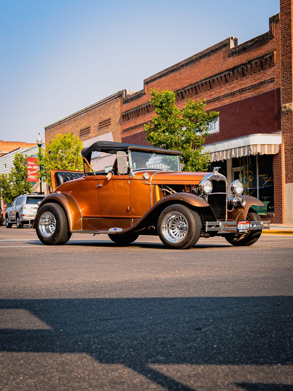 Orange vintage hot rod parked in front of brick buildings