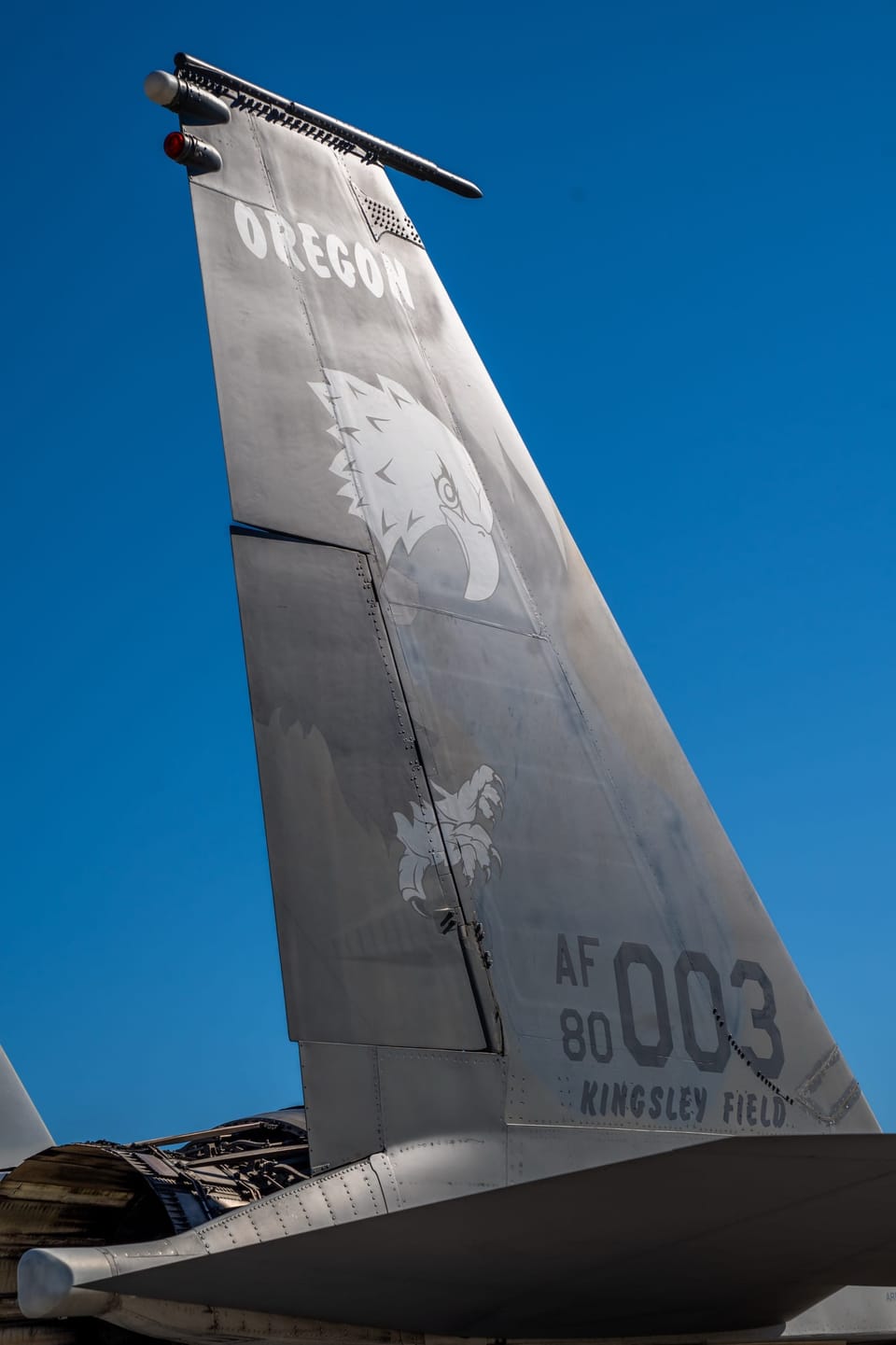 Tail fin of a gray military jet against a deep blue sky